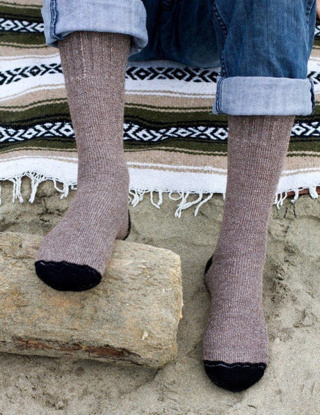 close up of a pair of feet wearing the cocoa brown alpaca adventure socks on a striped blanket on the beach