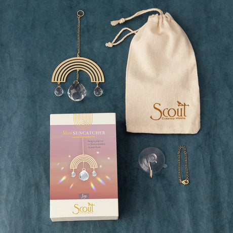 all of the rainbow mini suncatcher parts and packaging: the rectangular gift box, the muslin bag,  suction cup, hanging chain, and the mini rainbow suncatcher on a blue surface