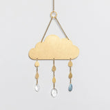 an elegant and minimal suncatcher in brass in the shape of a simple cloud with 3 gems hanging below it mimicking raindrops