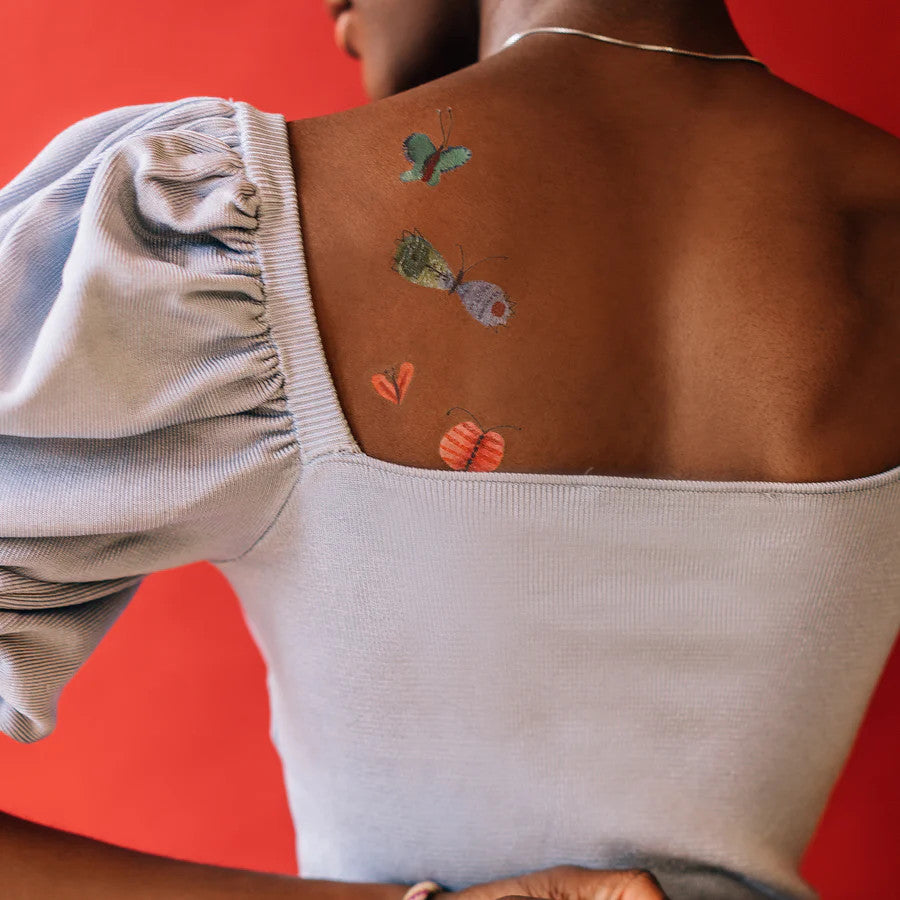 a model's back with a few of the colorful butterfly tattoos applied to her upper back and shoulder