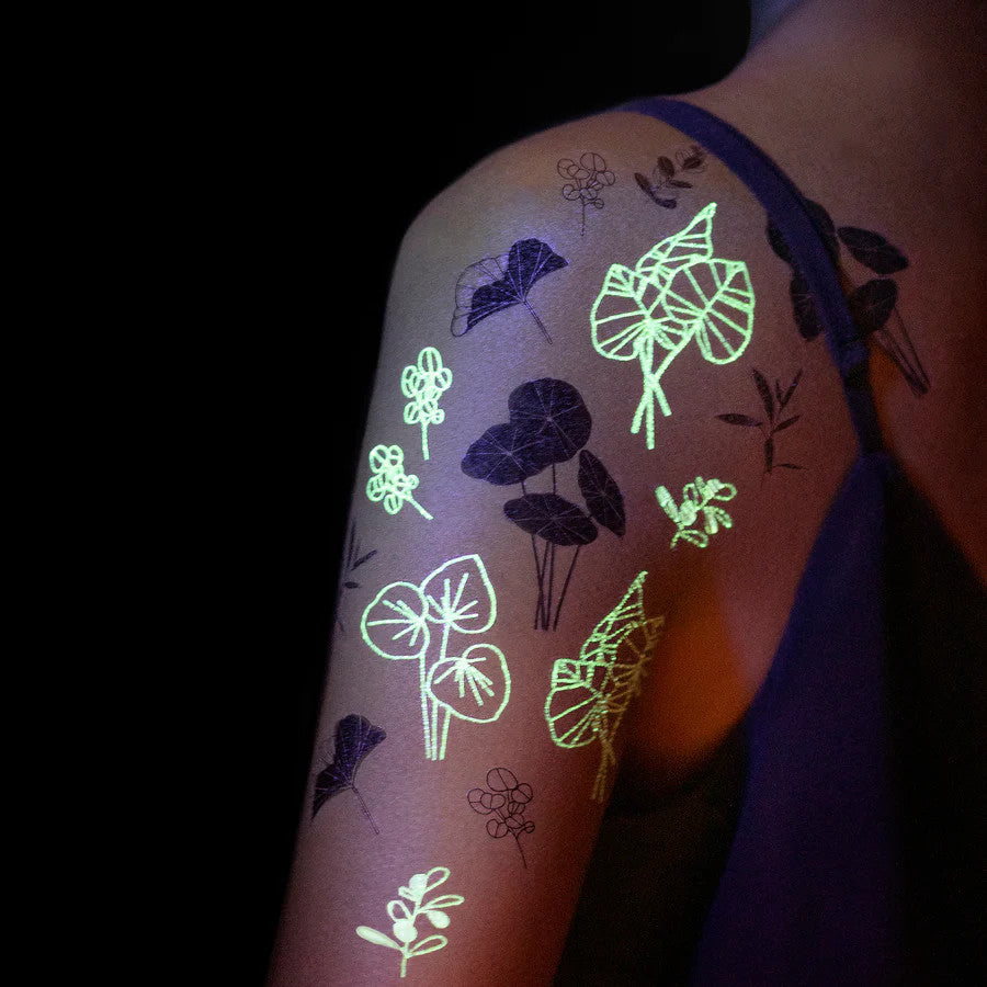 a dark room with a model's upper arm and shoulder with the glowing garden glow-in-the-dark tattoos applied showing how they glow in the dark