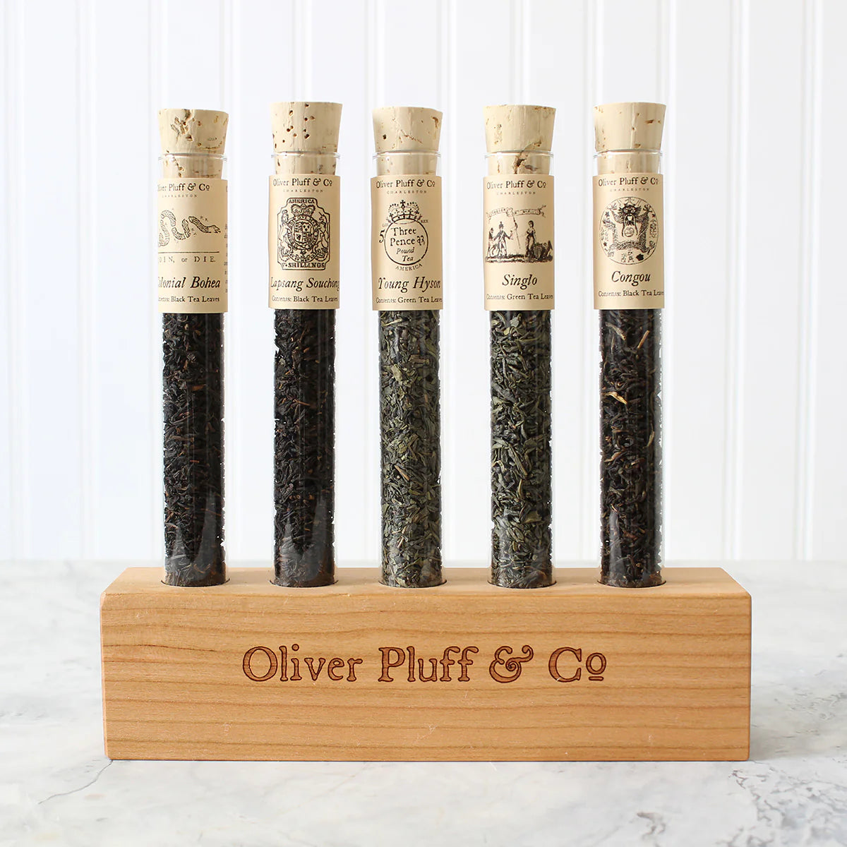 5 corked glass tubes of loose leaf tea blends on a wood display block with the brand "Oliver Plufff & Co on the front of it
