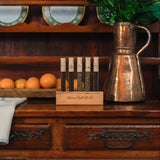 The teas of the Boston Tea Party in their display block on a colonial era kitchen hutch alongside a copper pot and plate of oranges
